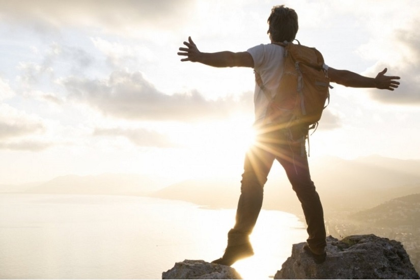 جوان موفق هنگام طلوع آفتاب روی یک صخره ایستاده