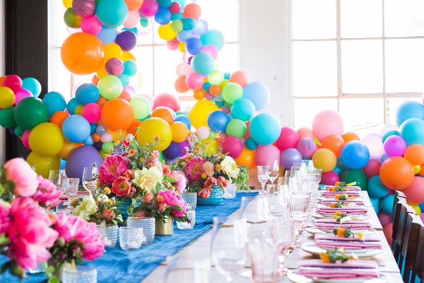 میز جشن تولد همراه با گل صورتی طبیعی و بادکنک‌های رنگارنگ